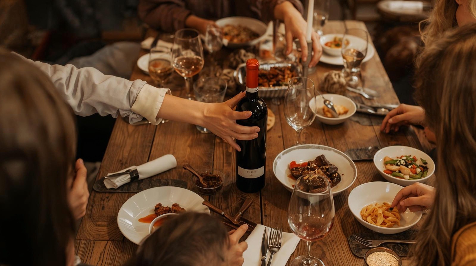 A full-screen, beautiful photo of diverse, happy friends enjoying a meal outdoors at a long table during sunset.